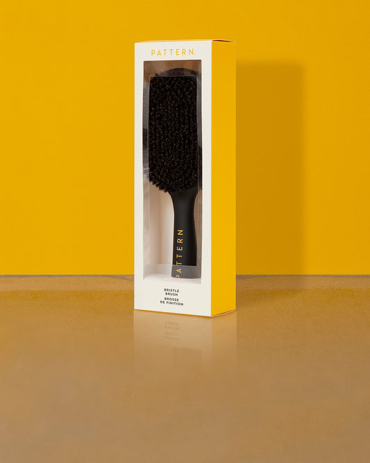Double-Sided Bristle Brush - Black rectangular double-sided bristle brush with a black handle in yellow and white PATTERN Beauty box.