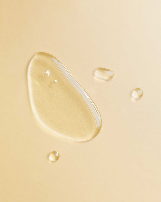 Argan Oil Blend - Clear golden argan oil droplets on a soft beige background, highlighting smooth texture and fluidity.