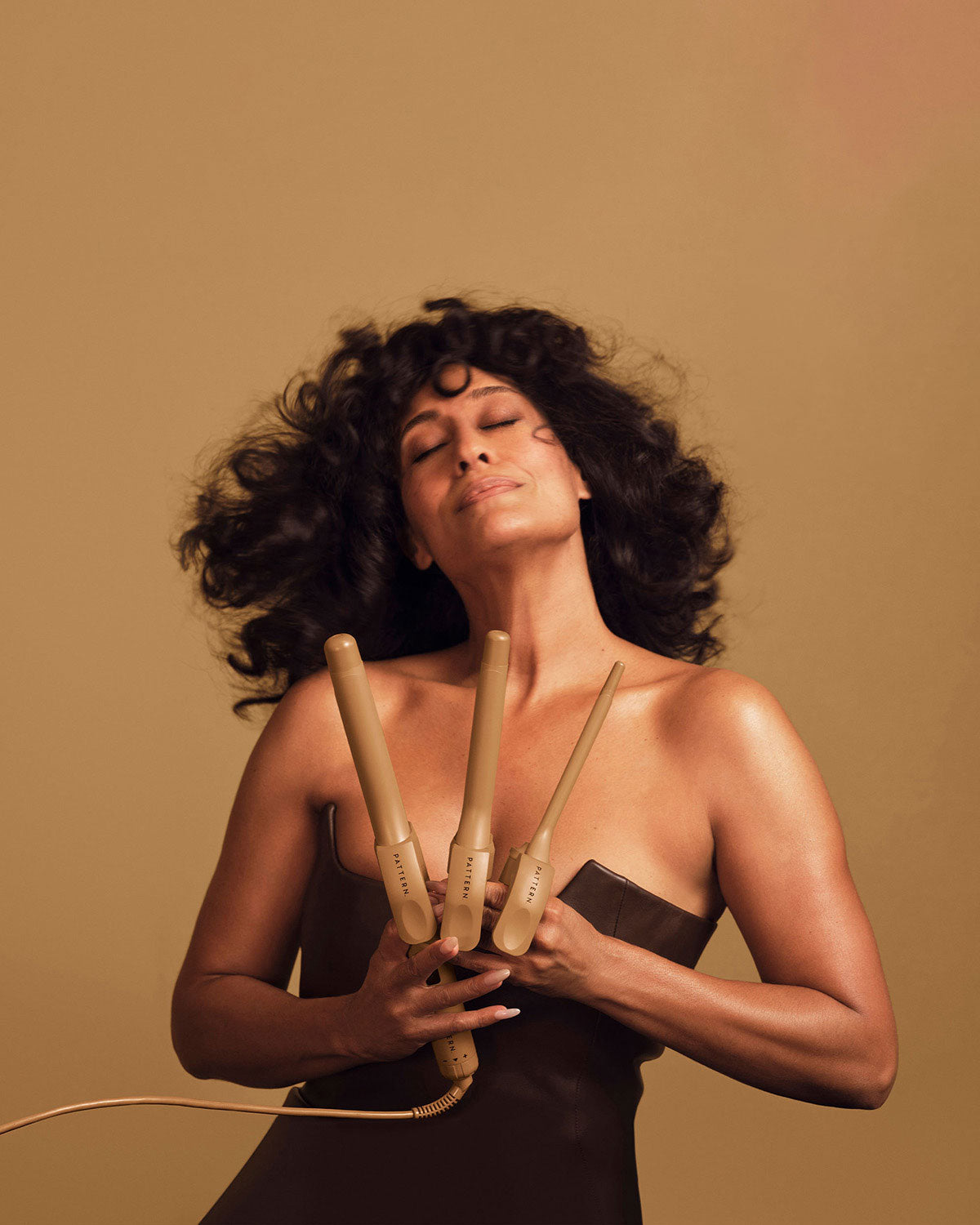 Woman holding wooden hair rollers against a brown background