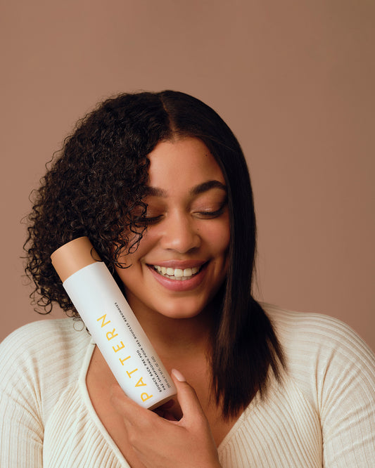 Bounce Back Pre-Poo - PATTERN Beauty Bounce Back Pre-Poo bottle held by smiling woman with curly and straight hair on beige background.