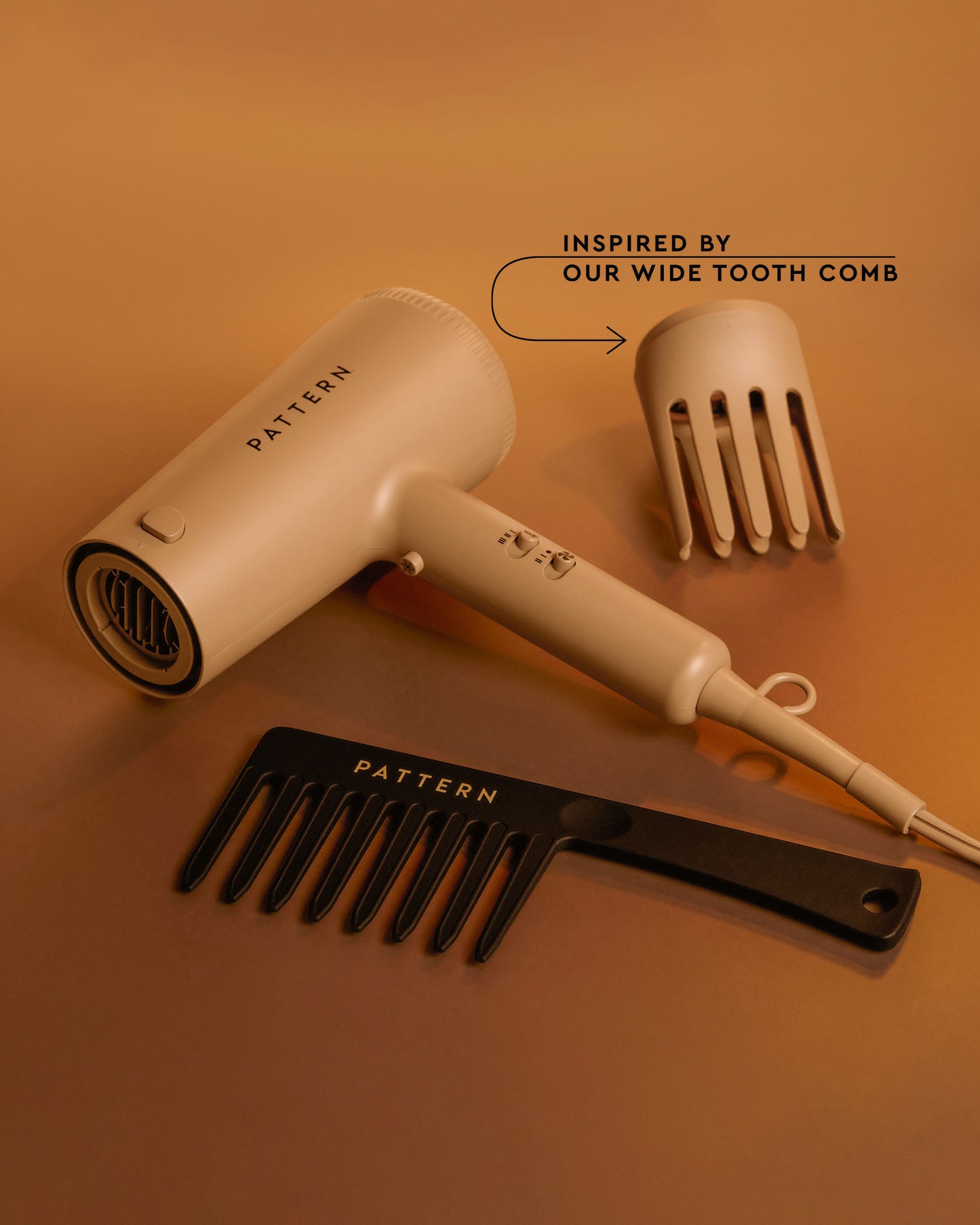 The PATTERN Blow Dryer - Beige PATTERN Beauty by Tracee Ellis Ross blow dryer with wide-tooth comb attachment and black wide-tooth comb on tan.