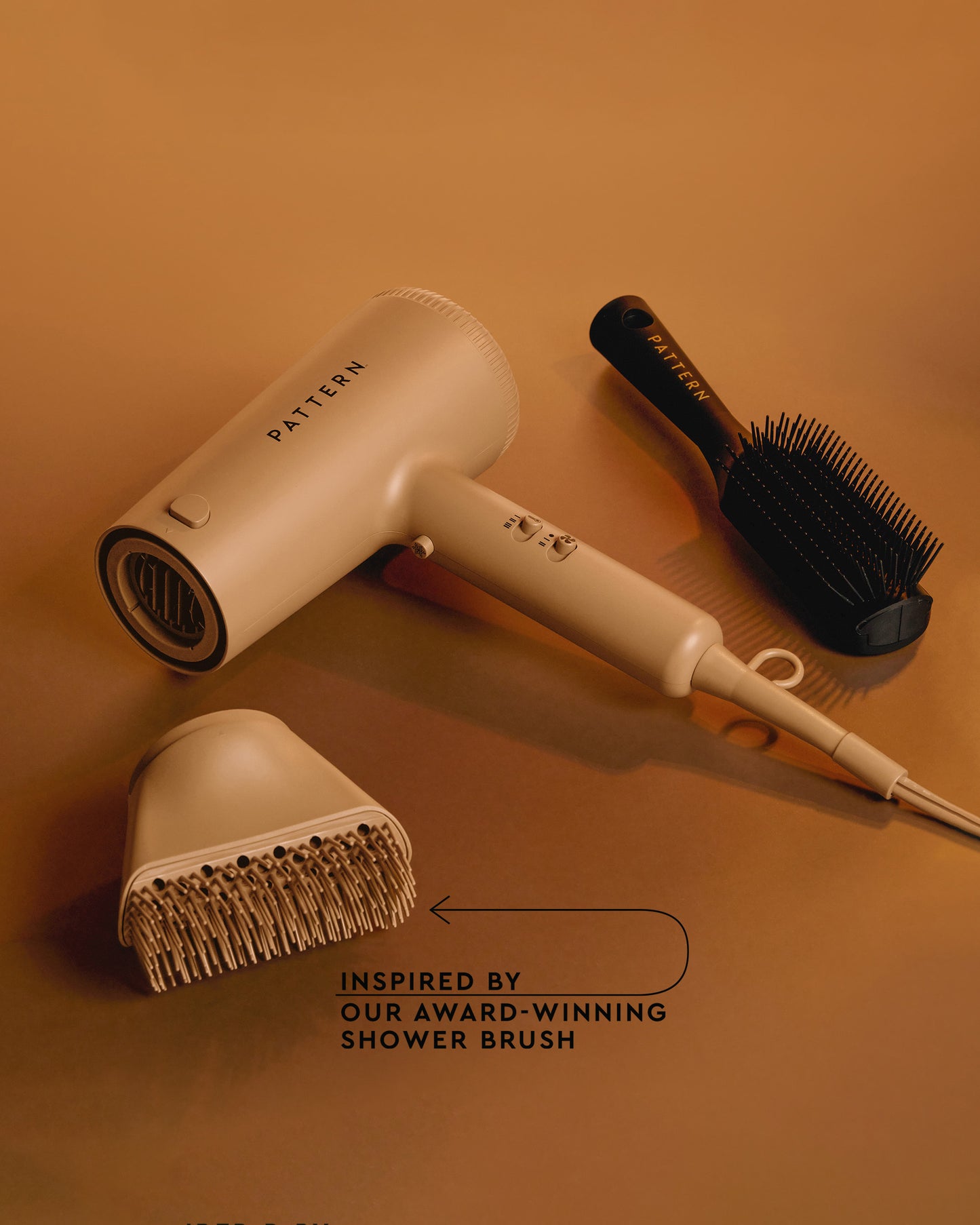 The PATTERN Blow Dryer - Beige PATTERN Beauty Blow Dryer by Tracee Ellis Ross with matching hair diffuser and black detangling brush on tan background.