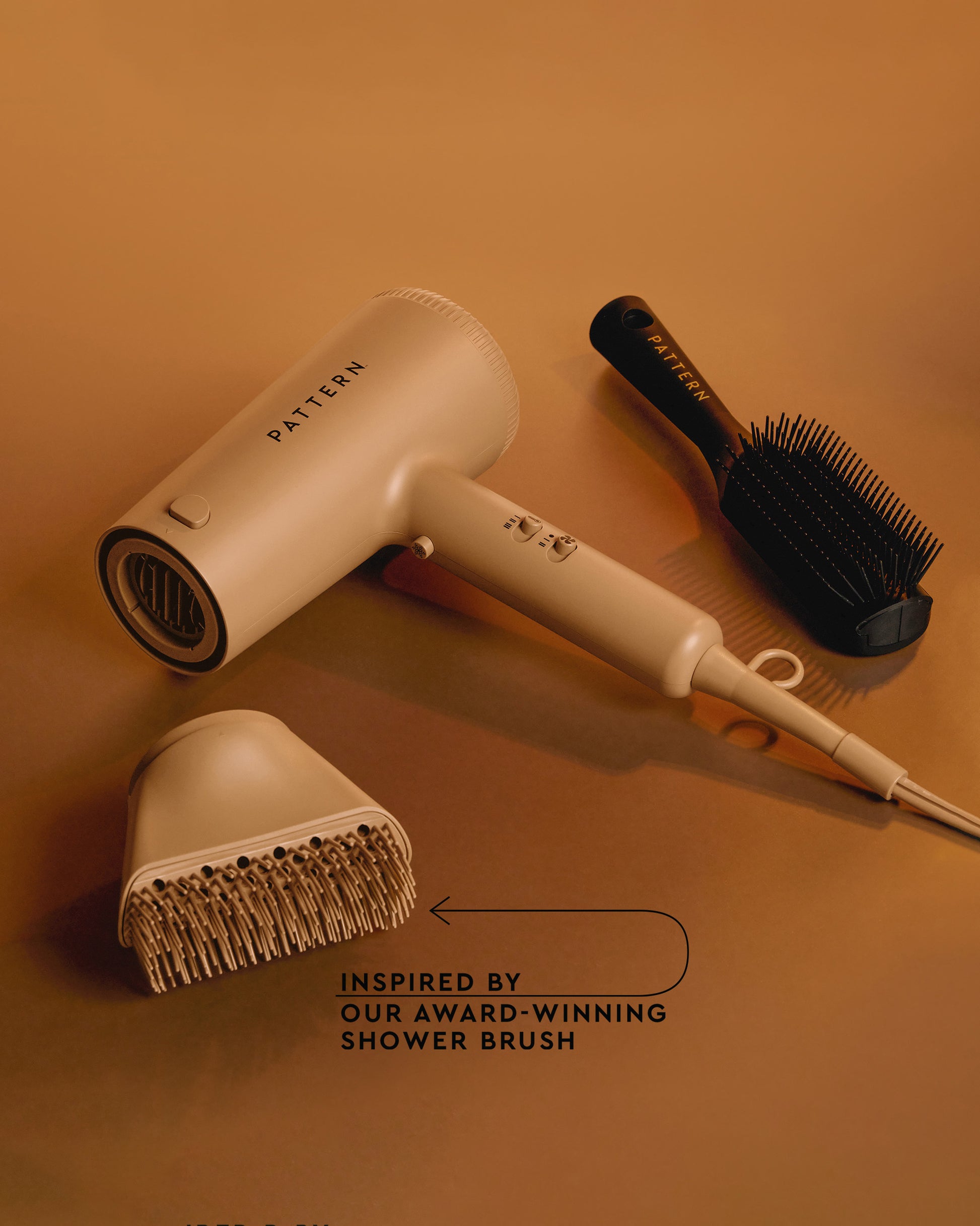 The PATTERN Blow Dryer - Beige PATTERN Beauty Blow Dryer by Tracee Ellis Ross with matching hair diffuser and black detangling brush on tan background.