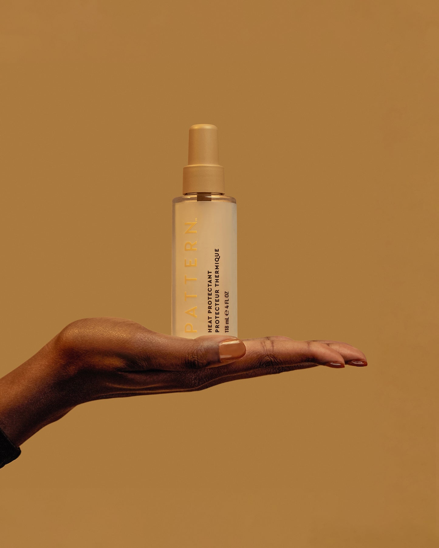 The Curling Iron & More Bundle - PATTERN Beauty by Tracee Ellis Ross curly hair spray in amber bottle held on outstretched hand against tan background.