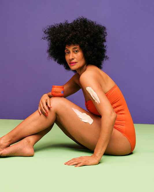 Moisture Rich Body Cream - Woman with curly hair wearing orange swimsuit applying PATTERN Beauty by Tracee Ellis Ross Moisture Rich Body Cream on arm.