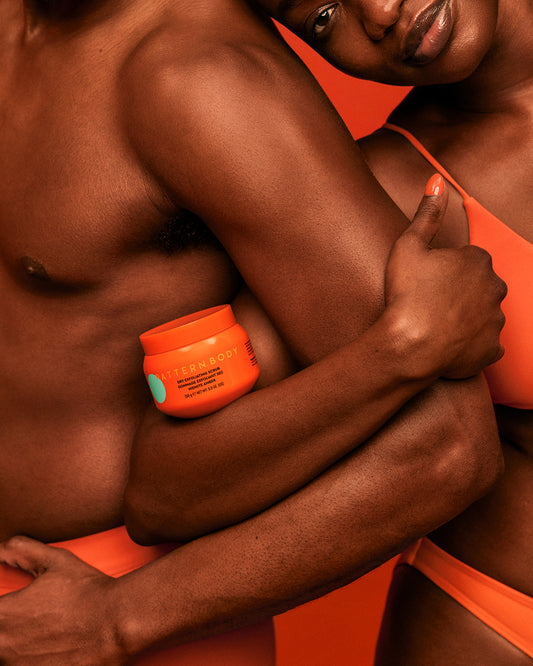 Dry Exfoliating Body Scrub - PATTERN Beauty by Tracee Ellis Ross dry exfoliating body scrub jar held by two models in orange swimwear against orange.