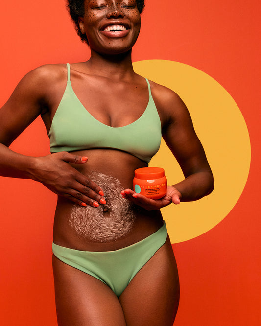 Dry Exfoliating Body Scrub - Woman in green bikini applying PATTERN Beauty by Tracee Ellis Ross Dry Exfoliating Body Scrub with orange jar and visible.