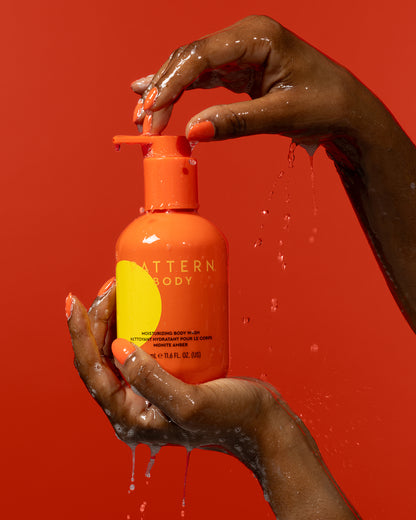 Moisturizing Body Wash - Orange bottle of PATTERN Beauty by Tracee Ellis Ross moisturizing body wash held by wet hands with water droplets.