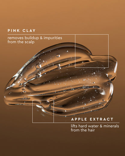 A glossy brown translucent cosmetic smear on a brown gradient background with white text reading 'PINK CLAY' and 'APPLE EXTRACT' plus descriptive claims about scalp and hair buildup.