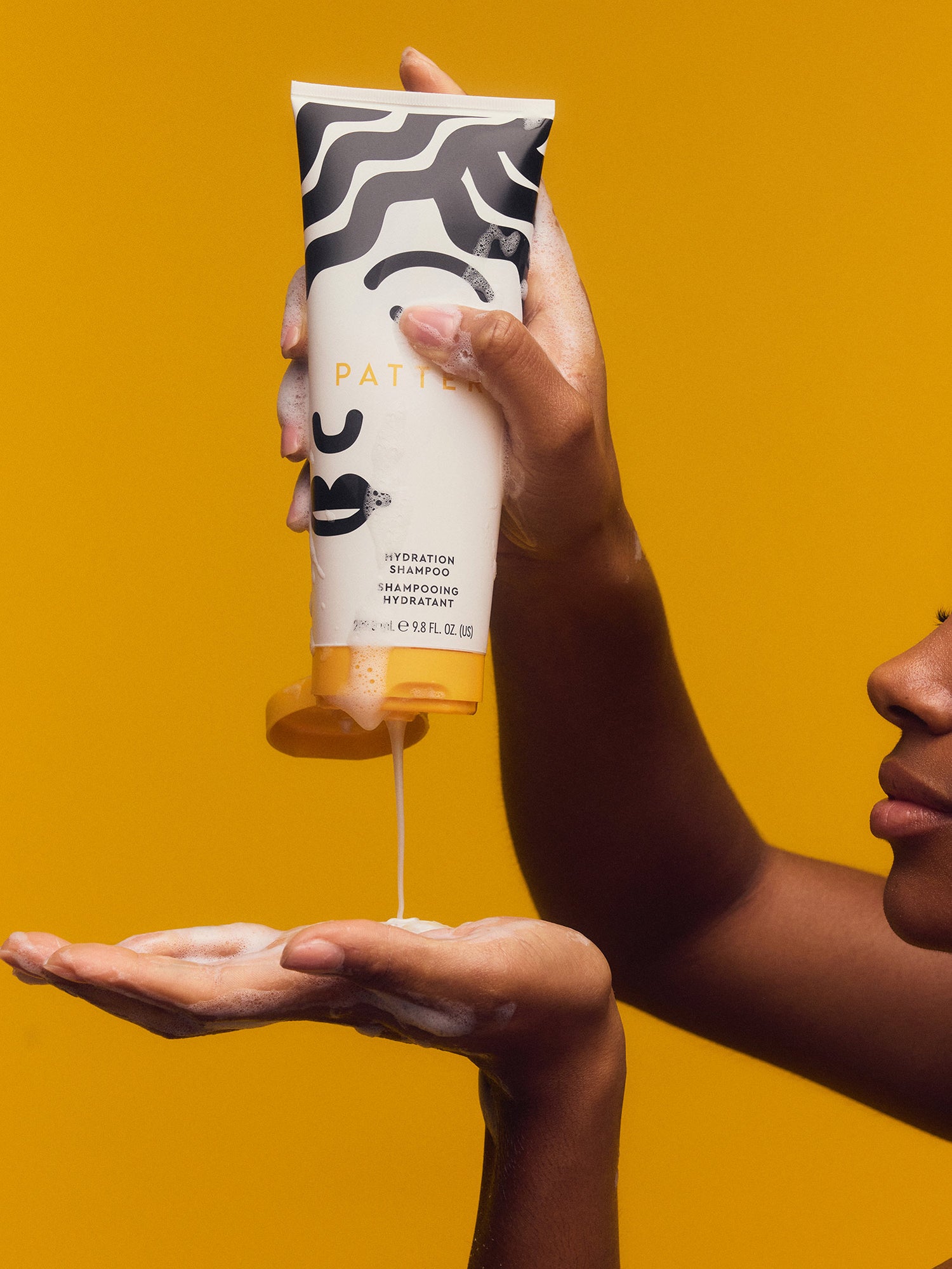 Person pouring a white tube of Patagonia body wash into their hand against a yellow background