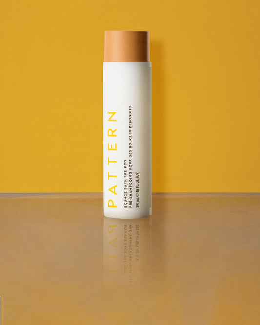 Bounce Back Pre-Poo - White cylindrical bottle with tan cap, labeled PATTERN Bounce Back Pre-Poo by Tracee Ellis Ross against a yellow background.