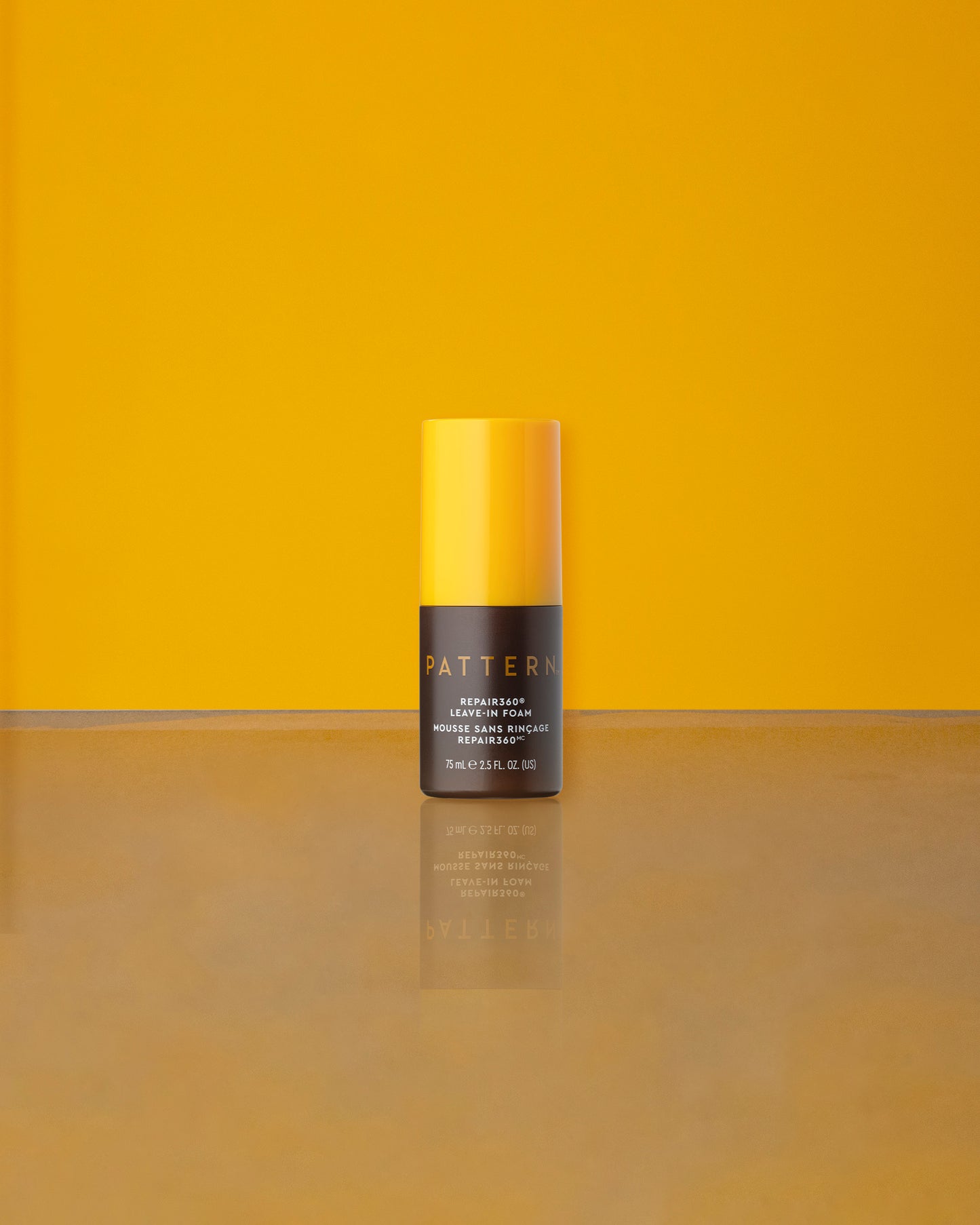 Repair360®  Leave-in Foam - PATTERN Beauty Repair360® Leave-in Foam bottle with yellow cap on reflective surface against yellow background.