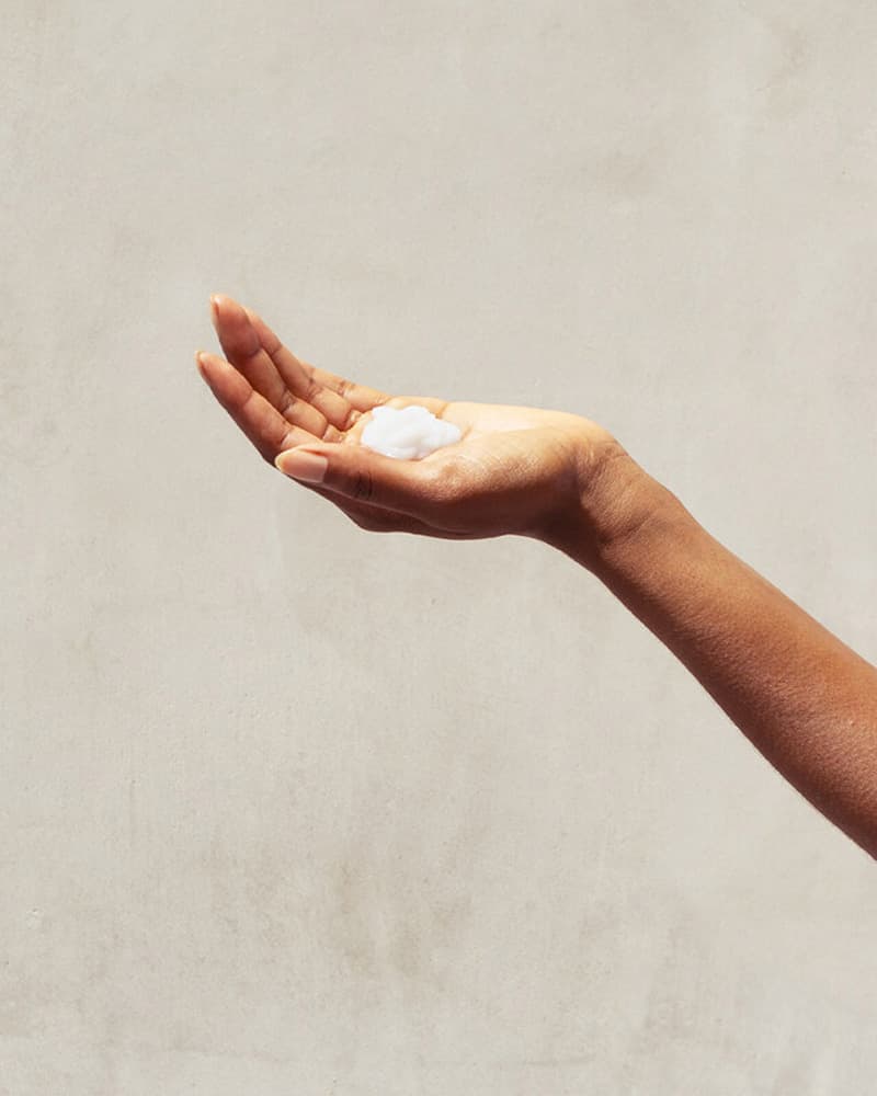 Leave-In Conditioner - A hand holds a small amount of white PATTERN Beauty leave-in conditioner against a neutral background.