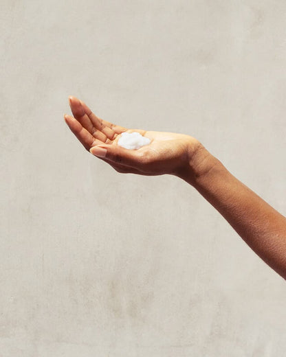 Leave-In Conditioner - A hand holds a small amount of white PATTERN Beauty leave-in conditioner against a neutral background.