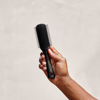 Mini Shower Brush - Black Mini Shower Brush with fine teeth and ergonomic handle held in hand, PATTERN Beauty by Tracee Ellis Ross branding.